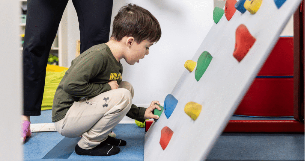 Child participating in occupational therapy activities using an indoor climbing wall to develop motor skills and coordination.